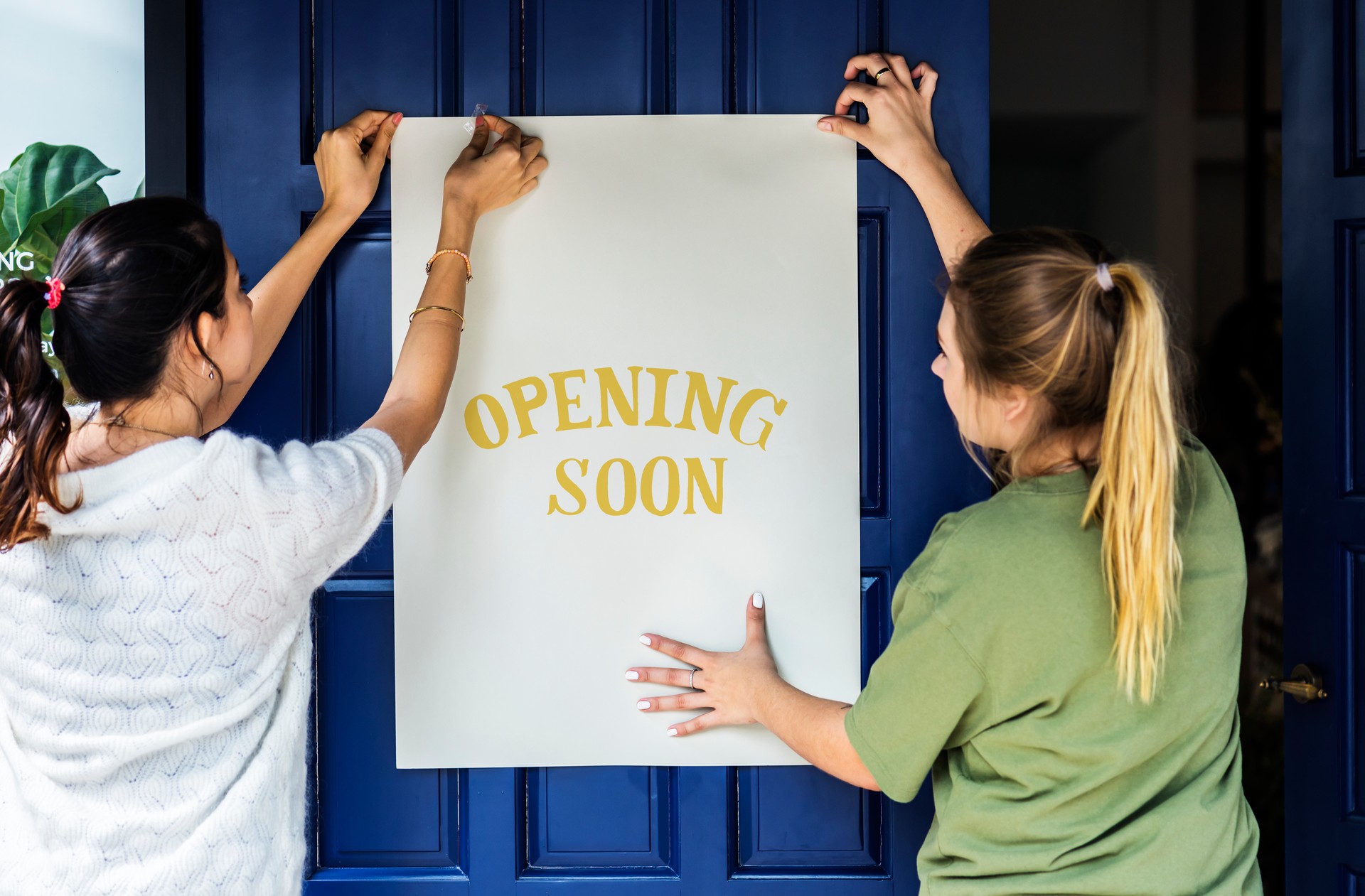 Women putting on store opening soon sign